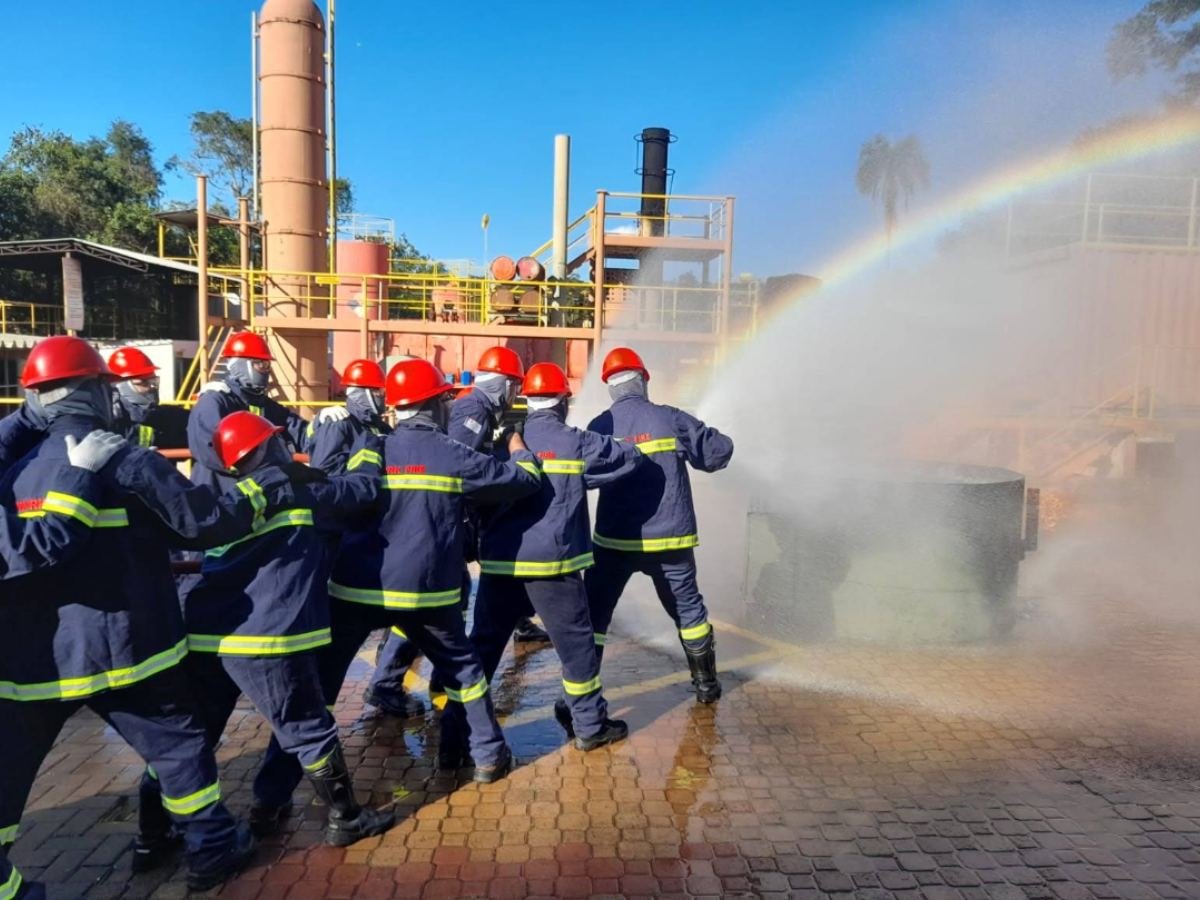 Equipe com mangueira em treinamento, com arco-íris na névoa d'água